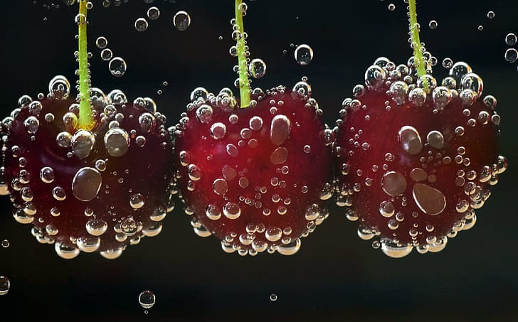 Fresh cherries suspended in sparkling water against a deep black background